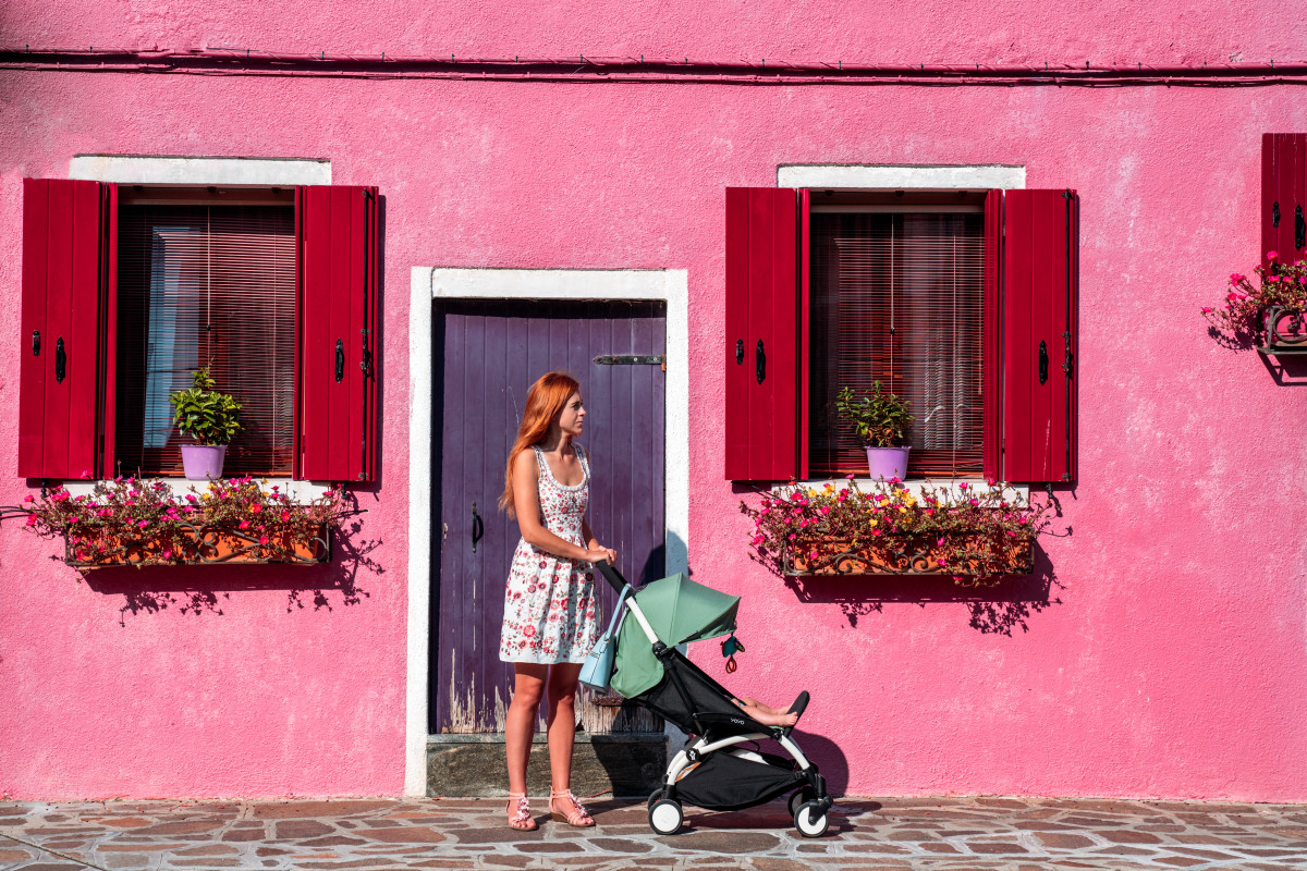 Woman with a travel stroller in front of a vibrant pink house, illustrating the challenges of mobility when flying with a baby.