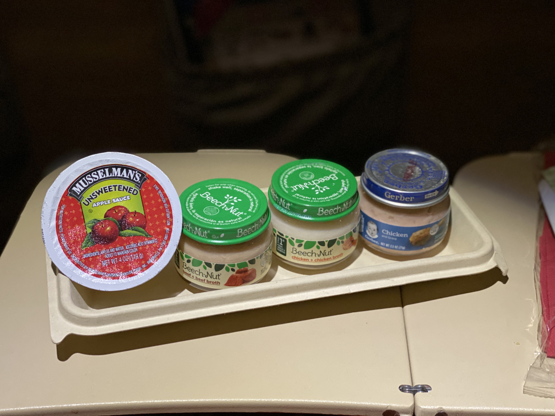 An airplane tray table showing baby meals on planes, essential for keeping a little one content when flying with a baby.